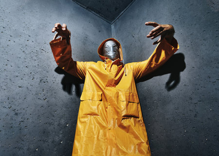 Giant scary man with duct tape face wrap in bright yellow raincoat looking down to camera standing in the corner of the room. Horror conceptの写真素材