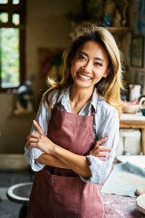 Pretty female artist smiling and posing at creative workshop with her artwork in the background.. Success, art conceptの写真素材