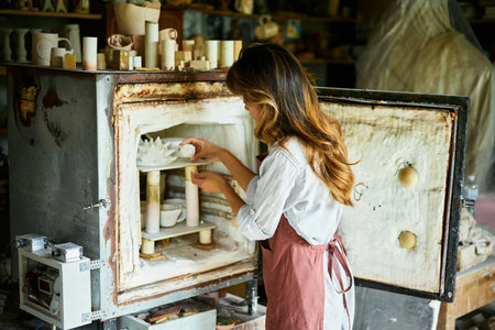 Female artist placing her ceramic clay crafts at pottery kiln. Mastering the art of pottery craft ceramicsの写真素材