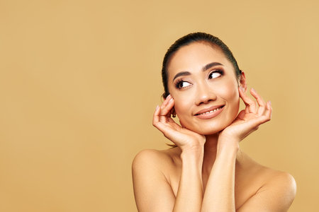 Beautiful smiling woman portrait on beige background looking aside on copy space.の写真素材