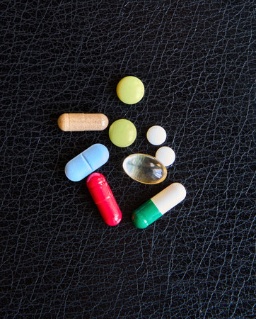 Various pills and vitamins of different colors and shapes on black background. Medicine, healthcare...