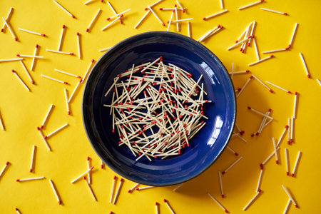Collection of red-tipped wooden matches in dark blue bowl over bright yellow backgroundの写真素材