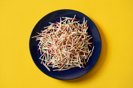 Collection of red-tipped wooden matches in dark blue plate over bright yellow backgroundの写真素材