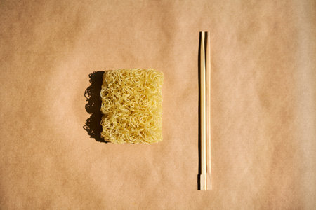 Dry instant noodles with wooden chopsticks on brown background. Flat lay, Asian food conceptの写真素材