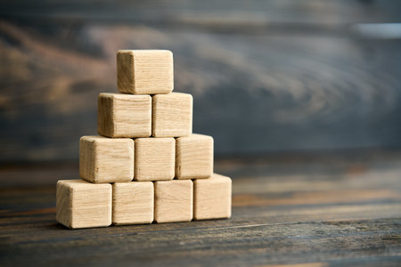 Stack of natural wooden cubes arranged in pyramid shape with copy space over dark wooden backgroundの写真素材