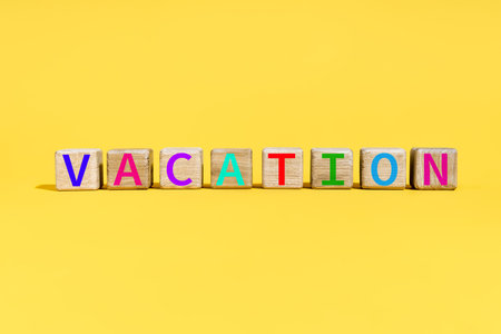 The word VACATION on wooden blocks on vibrant yellow background with colorful letters.の写真素材
