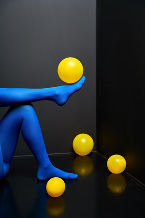 Woman legs in blue tights and elegant shoes lying on black floor among yellow balloons. Party, relax conceptの写真素材