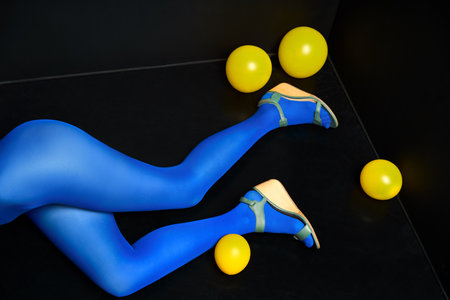 Woman legs in blue tights and elegant shoes lying on black floor among yellow balloons. Party, relax conceptの写真素材