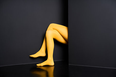 Female legs in yellow tights and elegant sandals emerging from black wall backgroundの写真素材