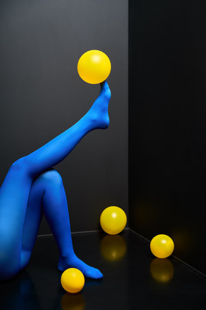 Woman legs in blue tights and elegant shoes lying on black floor among yellow balloons. Party, relax conceptの写真素材