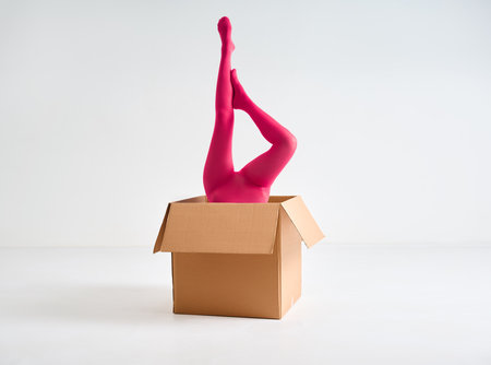 Female legs in bright pink tights raised up from open cardboard box over white studio backgroundの写真素材