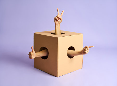 Multiple hands making peace, thumbs up, and pointing gestures from holes in cardboard box.