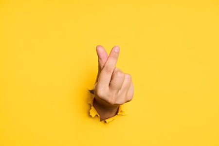 Love finger gesture through hole in torn yellow paper background