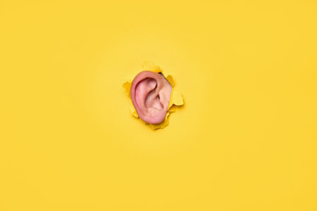 Close-up of human ear through torn yellow paper. Curiosity, secret concept