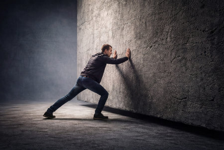 Strong man struggling to push moving massive stone wall in dark dramatic atmosphere. Generative AIの素材