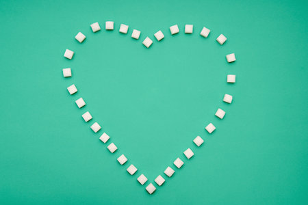 Heart shape created from sugar cubes on green background. Love, sweets concept