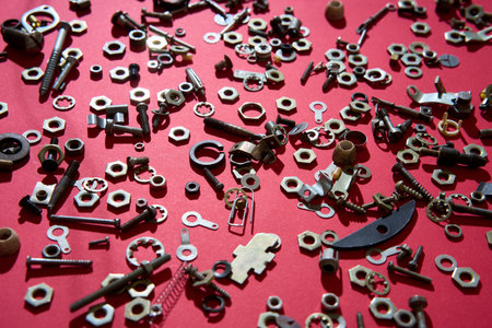 Assorted metal screws nuts and bolts on red background creating industrial hardware texture