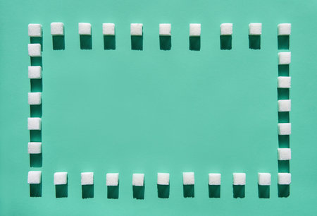 Minimal creative layout of sugar cubes forming square frame on green pastel background