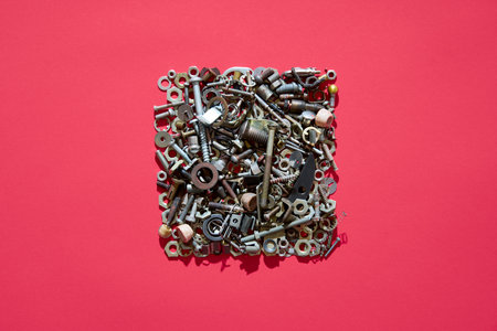 Square arrangement of mixed screws nuts and bolts on red background creating industrial concept