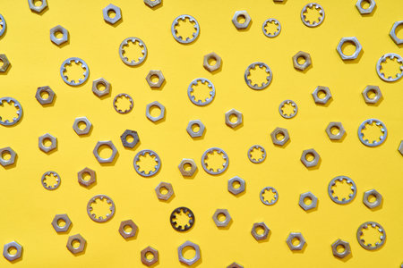 Assorted metal washers and nuts scattered on yellow background