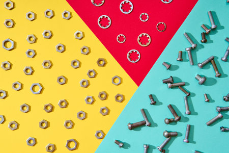 Metal nuts bolts and washers arranged on colorful geometric background with yellow red and mint sections