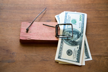 Stack of hundred dollar bills caught in a wooden mousetrap representing financial trap, bankruptcy concept
