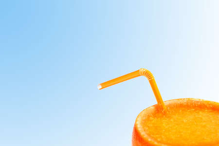 orange juice in the skin of an orange with a tube on the blue . concept of natural juicesの写真素材