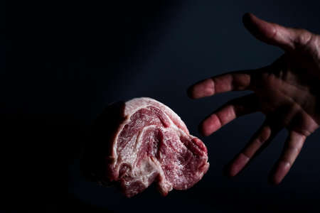 man hand and piece redraw pork neck meat on dark backgroundの写真素材