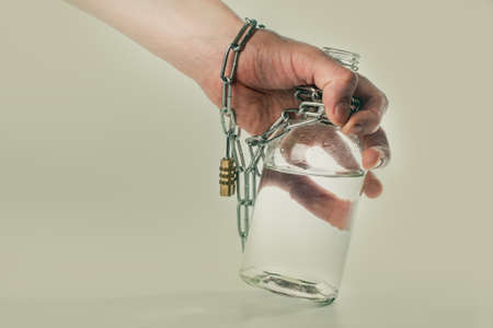 man's hand connected with bottle of alcohol with a metal chain on beige backgroundの写真素材