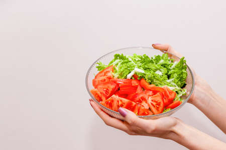 in the hands of girls glass bowl, in which green leaves salad half with red tomatoesの写真素材