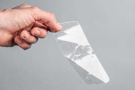 man holds broken, broken smartphone safety glass in hand on grey background. concept of fragile...
