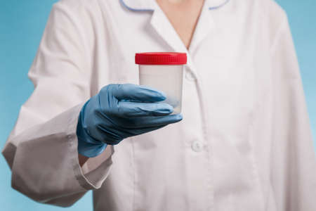 doctor in a white uniform and blue gloves on blue background holds an empty plastic test jarの写真素材