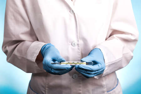 portrait of a young woman doctor on a blue background who looks at the thermometer and worries. high...