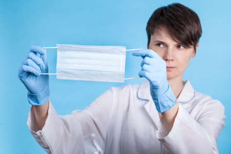 doctor in a white medical coat and blue gloves shows a medical mask. concept of protection from the...