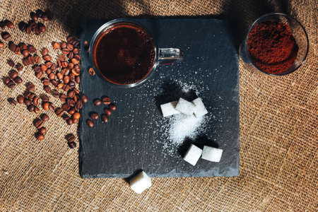 black coffee in a transparent glass Cup on a background of burlap. next to sugar, coffee beans and ground coffee. the view from the topの写真素材