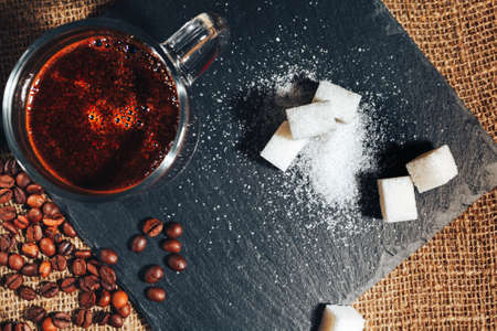 black coffee in a transparent glass Cup on a background of burlap. next to sugar, coffee beans and ground coffee. the view from the topの写真素材