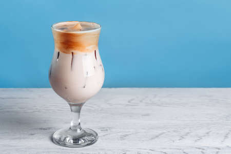 Dalgona korean Iced Coffee, a trendy fluffy creamy whipped coffee with ice on a white wooden table....