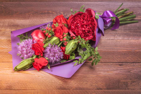 bouquet with red flowers in purple packaging on wooden background. high quality. bright sunlightの写真素材