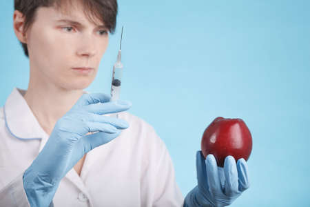 Portrait of a female doctor standing with an Apple and a syringe on a blue background as the idea of...