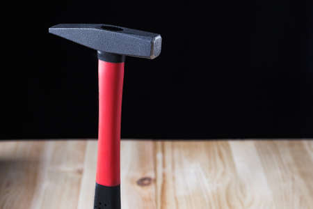 nail hammer stands on a wooden table against a black background. high quality, beautiful color, high...
