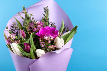 bouquet of flowers with tulips and anemones in a lilac package on a blue background. close-up, high quality.の写真素材