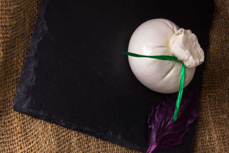 One Mozzarella cheese, basil over old black burlap background on black stone slate close upの写真素材