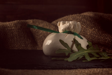 One Mozzarella cheese over old black burlap background on black stone slate close upの写真素材