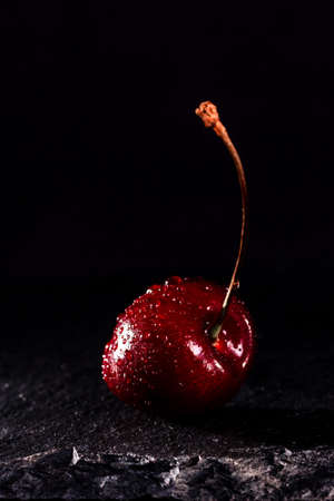 one red cherry with water drops on black stone background