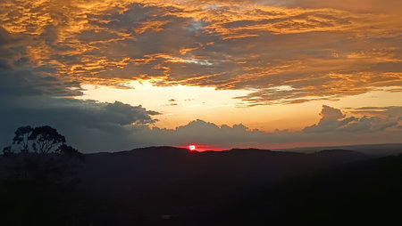 beautiful orange sunset sky and clouds with mountains and trees in silhouetteの写真素材