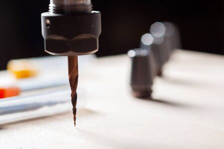 spindle with a cnc router mill over a wooden surface, against the background of three milling cutters in boxes and three colletsの写真素材