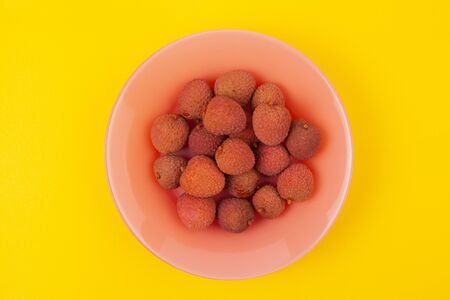 several lychee fruits lie on a coral plate on a yellow backgroundの写真素材
