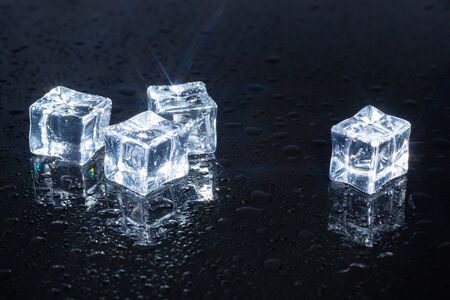 four ice cubes on black glass in water drops, used as a background