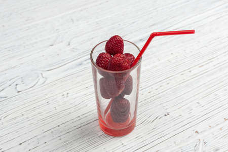 transparent glass with strawberries and red tuba on a wooden white table