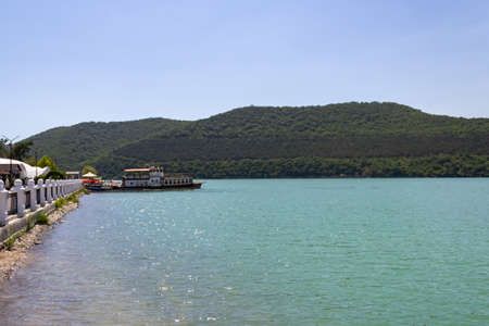 azure lake and pleasure boat on the wharf, in the background of the mountains covered with vegetationの写真素材